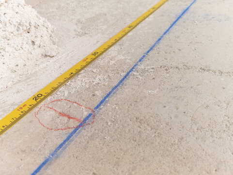 Close up photograph of a yellow measuring tape on a concrete floor with blue chalk line and red marking at a construction site