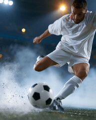 Naklejka premium Soccer player kicks ball with powerful motion. Dust rises under intense stadium lights. Athlete wears white kit, focused expression. Moment captures athletic skill and precision