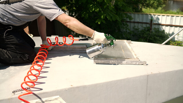 A worker in overalls uses an air spray gun to paint a metal hatch on a boat deck. Close up shot of professional painting and restoration work outdoors. DIY boat maintenance and repair