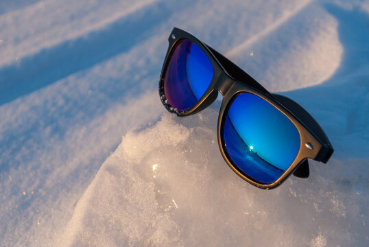 Sunglasses on snow and ice with blue mirrored lenses in bright winter sunlight
