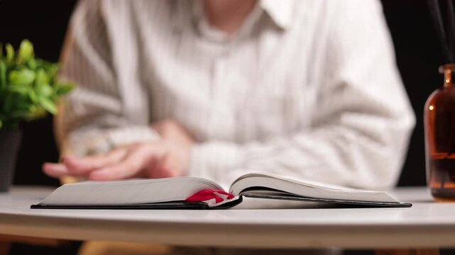 Person reading an open book with a red bookmark on a table