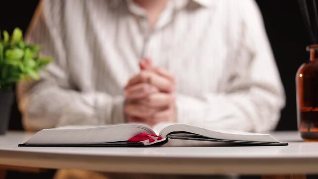 Person praying with open book and plant on table