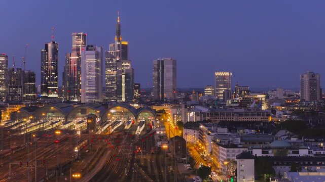 Aerial view of Hauptbahnhof and the illuminated skyline with skyscrapers and train tracks at twilight in Frankfurt am Main, Hessen, Germany.