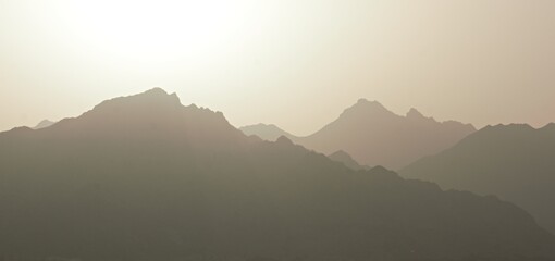 Obraz premium Majestic desert mountain layers in haze under bright sun, Saudi Arabia landscape