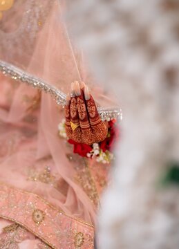 Closeup of indian bride hand with beautiful henna mehndi design holding a sheer pink veil