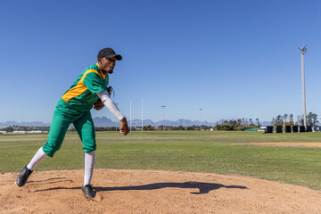 Obraz premium African American man pitching on dirt mound at field wearing green uniform and glove, copy space