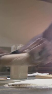 Vertical video: Close-up Kneading dough home baker rolling with pin at counter flour jar for baking