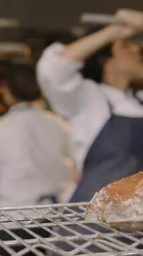 Vertical video: Placing loaf from peel, baker in chef coat cooling bread on wire rack, raising peel