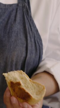 Vertical video: Tearing baker in denim apron revealing crumb on flour counter near rack, copy space