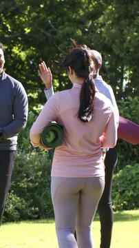 Vertical video: Coming woman in pink top gray leggings joining class in park with green purple mats