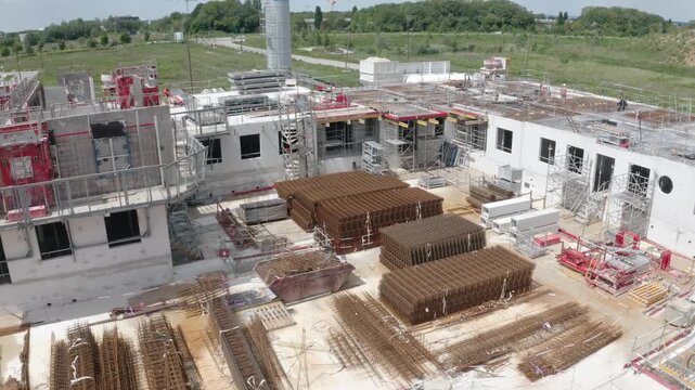Drone shot moving forward past the jib of a tower crane above a large urban construction site in daylight.