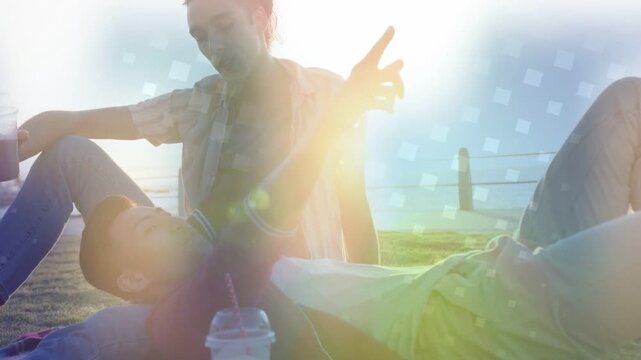 Lying man raising arm pointing at sunset, friend leaning, flare revealing faces for travel ad