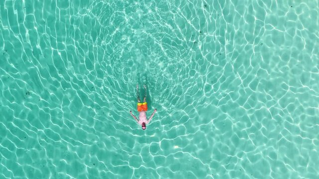 Aerial view of a man floating in the crystal clear turquoise water with sun ripples on the surface in Hoarafushi, Haa Alif, Maldives.