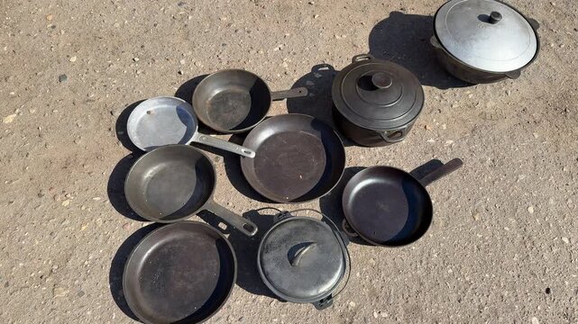 Used pans on asphalt at market sunlit cluster of assorted skillets and lids arranged for secondhand sale worn patina and rusty