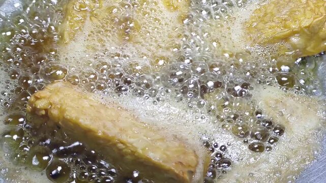 Tempeh slices deep frying in hot bubbling and foamy oil.