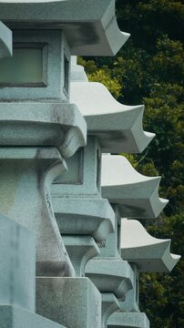 Close-up of traditional Japanese stone lanterns lined up in a row against lush green trees