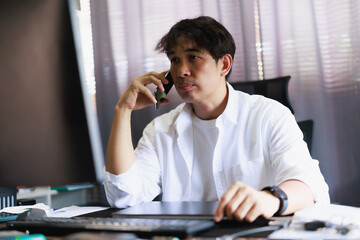 Fototapeta premium Asian man taking an important phone call, concentrating on the conversation and working from his home office, managing business remotely, communicating ideas and solutions