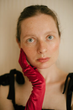 Elegant freckled woman in black dress and red gloves posing in vintage interior.