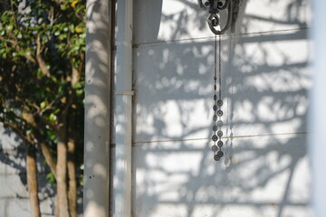 Obraz premium Metal decorative chain hanging from building edge casting sharp shadow on white wall, US Military Housing, Yangmingshan, Shilin District, Taipei, Taiwan, strong afternoon directional sunlight.
