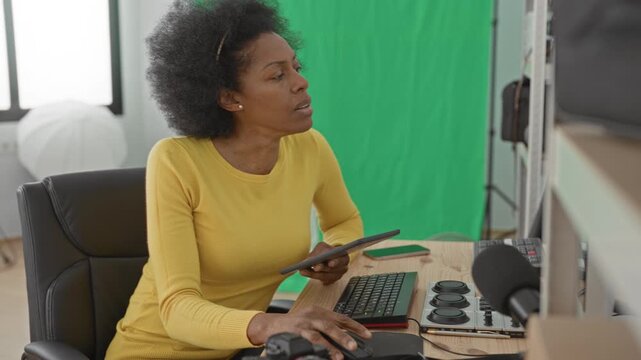 Woman tapping tablet and typing on keyboard in a green screen studio; concentration creativity focus production.