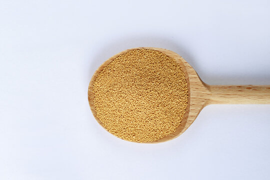 Dry active yeast granules in wooden spoon on white background, baking ingredient macro texture,