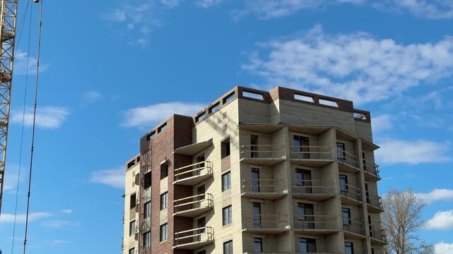 Unfinished apartment tower under blue sky, scaffolding and crane visible at left, concrete and brick facade with balconies