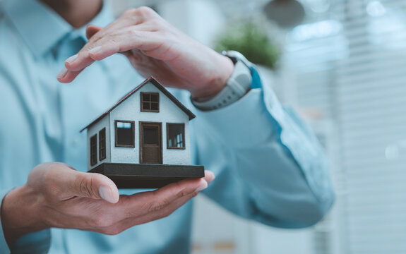Home insurance property protection risk management concept businessman hands making roof shape over miniature model house for real estate security family shelter safety