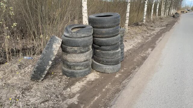 Stacked worn tires on gravel roadside. Birch trees background, columns of passenger car tires awaiting collection, weathered