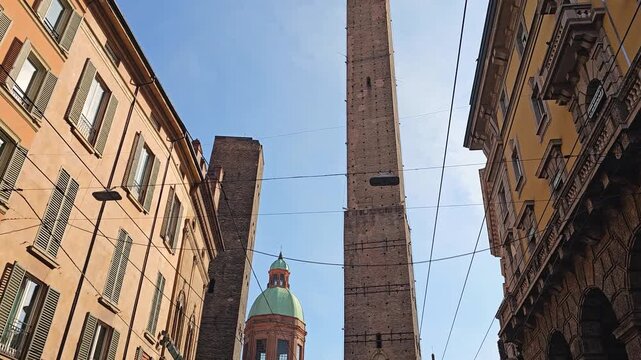 Street-level view of the Two Towers and historic buildings in Bologna, Emilia-Romagna, Italy, on a sunny day.