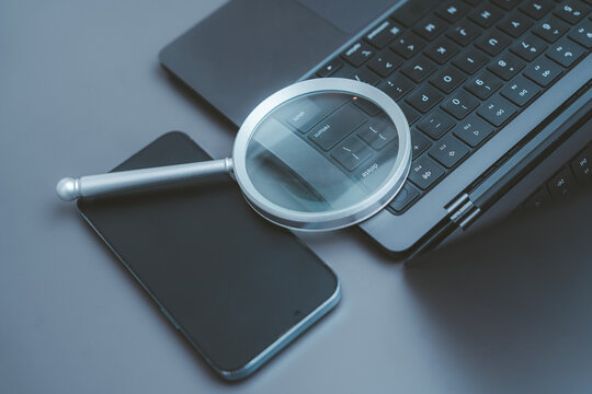 Digital forensics cyber security online search data investigation concept magnifying glass on laptop computer keyboard and blank screen smartphone internet finding software