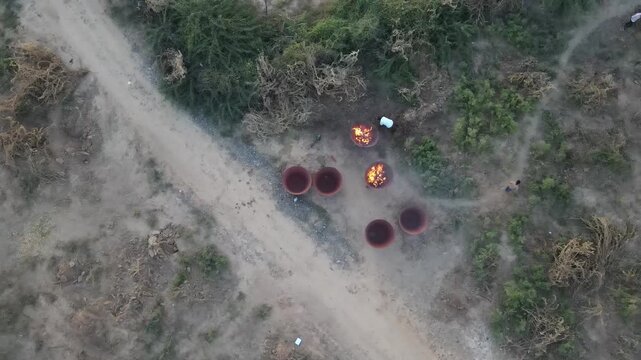 Cinematic drone view of traditional pottery kilns with burning firewood in a rural village, showcasing terracotta craftsmanship, smoke, fire, handmade ceramics, and countryside culture.