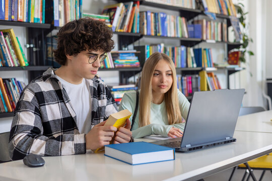 Teen students studying together in library with books and laptop, representing collaboration, tutoring, peer-to-peer learning and mentorship, exam preparation, language school learning, STEM, coding