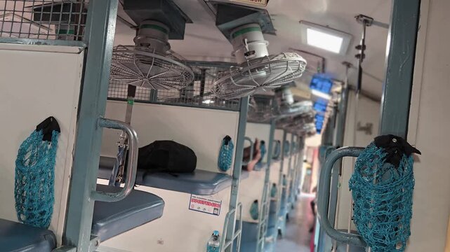 Sleeper coach interior of Indian Railways with blue berths for sleep and leisure. Metal ceiling fans & blue mesh bottle holders on frames offer pure comfort, encouraging quiet relaxation and deep rest