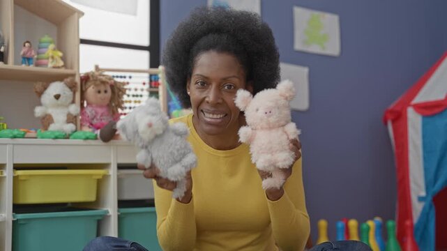 Woman holding two plush hand puppets while speaking in a colorful preschool classroom; playful learning.