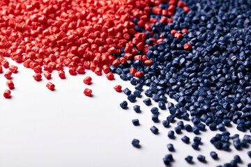 Fototapeta premium High-angle close-up shot of vibrant red and deep blue industrial plastic pellets scattered on a clean white background, showcasing raw materials for polymer manufacturing and chemical processing.