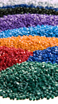 A wide assortment of colorful industrial plastic pellets and granules in vibrant shades of green, red, orange, blue, and purple, used as raw materials in polymer manufacturing and recycling.