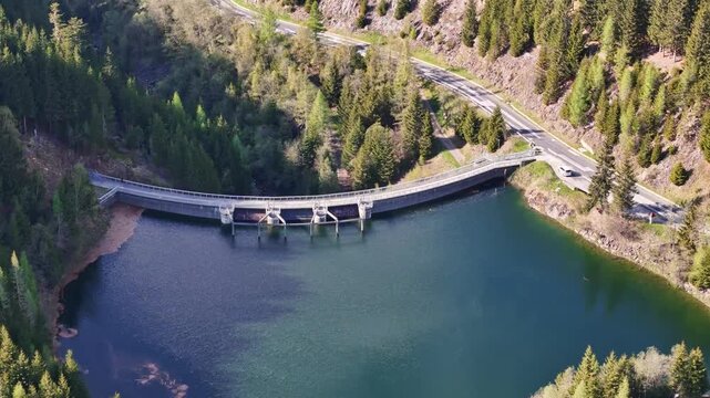Aerial view of Kraftwerk Bodendorf and Sperre Paal dam surrounded by dense evergreen forests and a winding mountain road Murau, Styria, Austria.
