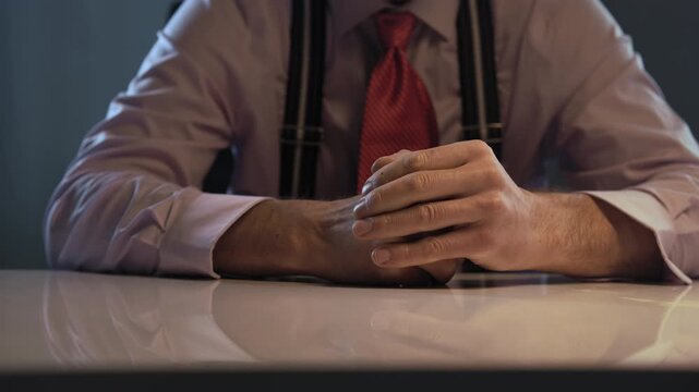 A businessman with restless hands at an office desk, wearing a pink shirt