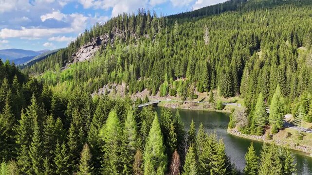 Aerial view of Kraftwerk Bodendorf and Sperre Paal dam surrounded by dense evergreen forests and rocky hills in Murau, Styria, Austria.