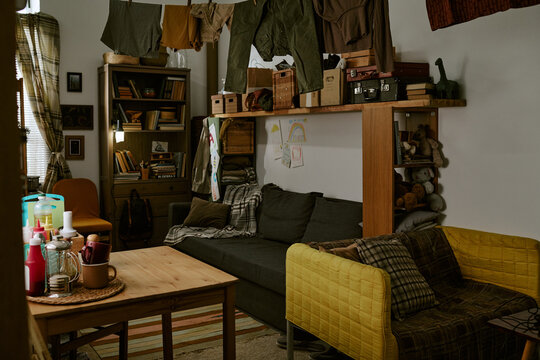 Wide shot of cluttered living room showing clothes drying indoors, packed shelves, worn seating, conveying poverty and cramped housing. Useful for housing crisis, low income lifestyle campaigns