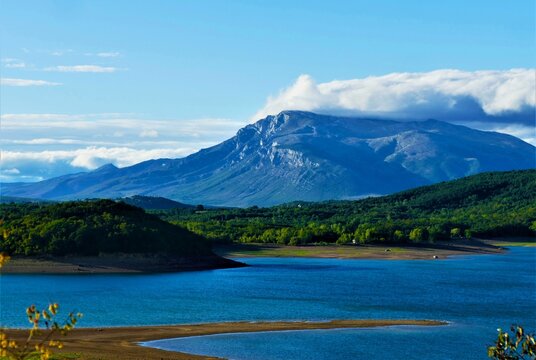 Big mountain by the lake with white clouds above and blue sky panoramic view