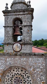 Aerial view of the stone bell tower and clock of Iglesia de Santa Marina de Augas Santas overlooking village rooftops in Augas Santas, Ourense, Spain.