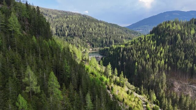 Aerial view of Kraftwerk Bodendorf and Sperre Paal dam surrounded by dense evergreen forests and mountain slopes in Murau, Styria, Austria.