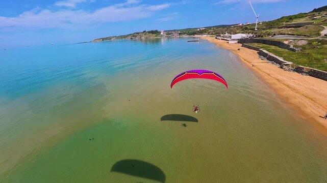 Aerial view of a paramotor flying over the turquoise waters and sandy shoreline of Kilyos beach with green hills under a clear blue sky Kumkoy, Istanbul, Turkey.