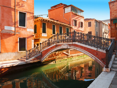 View of the narrow canal with colorful old houses and small footbridge in Venice on a sunny day, Italy.