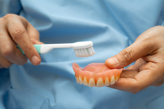 Asian senior woman patient clean teeth denture with toothbrush for chew food.