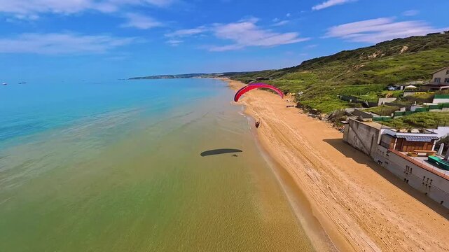 Aerial view of a red paramotor flying over the sandy Kilyos Beach with turquoise water and green hills in Kumkoy, Istanbul, Turkey.