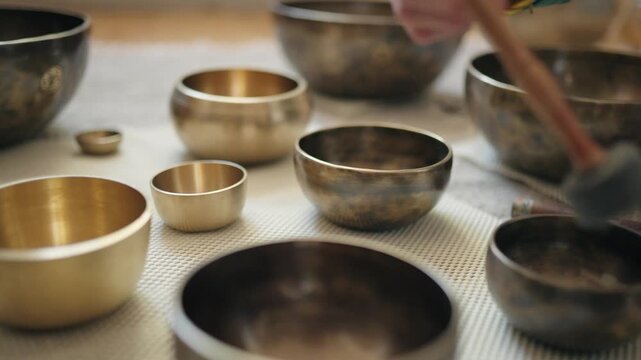A mallet strikes several Tibetan singing bowls one by one at eye level