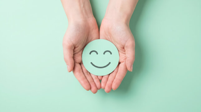 Closeup of hands holding a round paper cutout with a smiling face icon on a light green background, top view