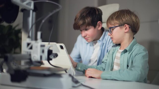 Boys at a table with a working 3D printer, observing and operating it by laptop
